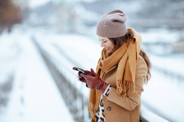 A woman in winter clothes uses her smartphone outdoors, emphasizing the importance of securing smart devices.